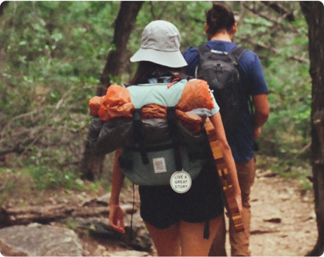 A woman hiking with a LIVE A GREAT STORY Luggage Tag on her backpack