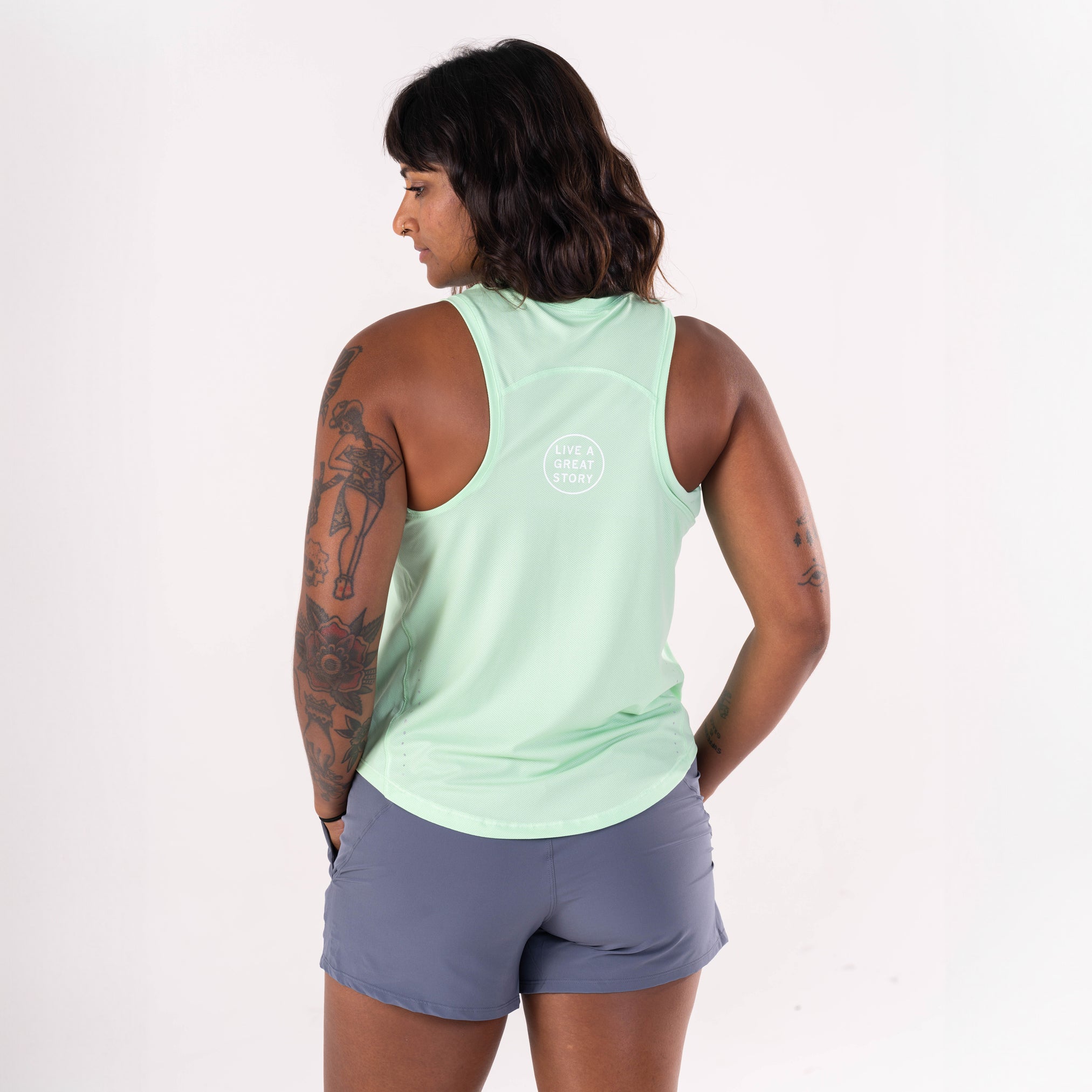 A woman wearing a green LIVE A GREAT STORY Women's Racer Tank Top