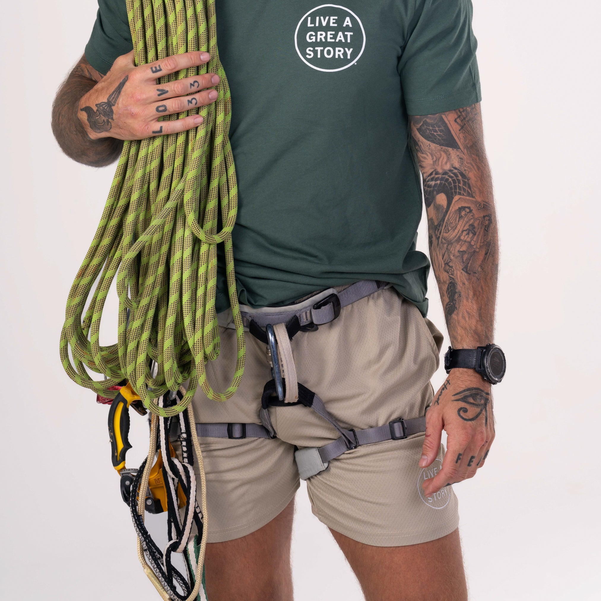 A man wearing light brown LIVE A GREAT STORY Men's Summer Shorts with a rock climbing harness over them