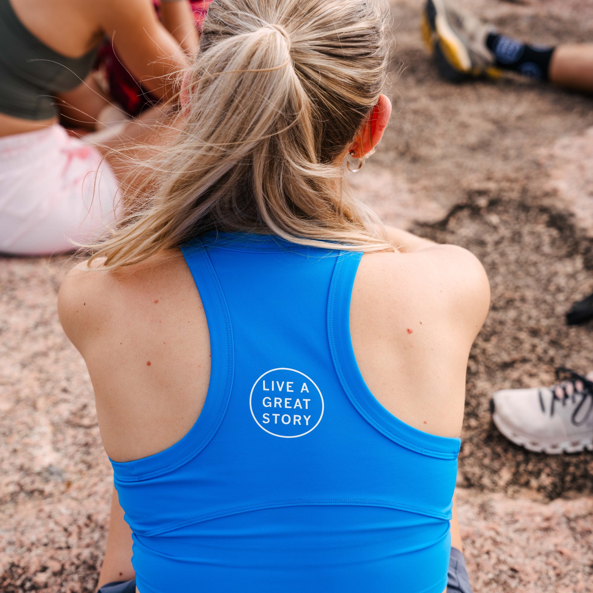 A closeup of woman wearing a blue LIVE A GREAT STORY women's tank top while outside