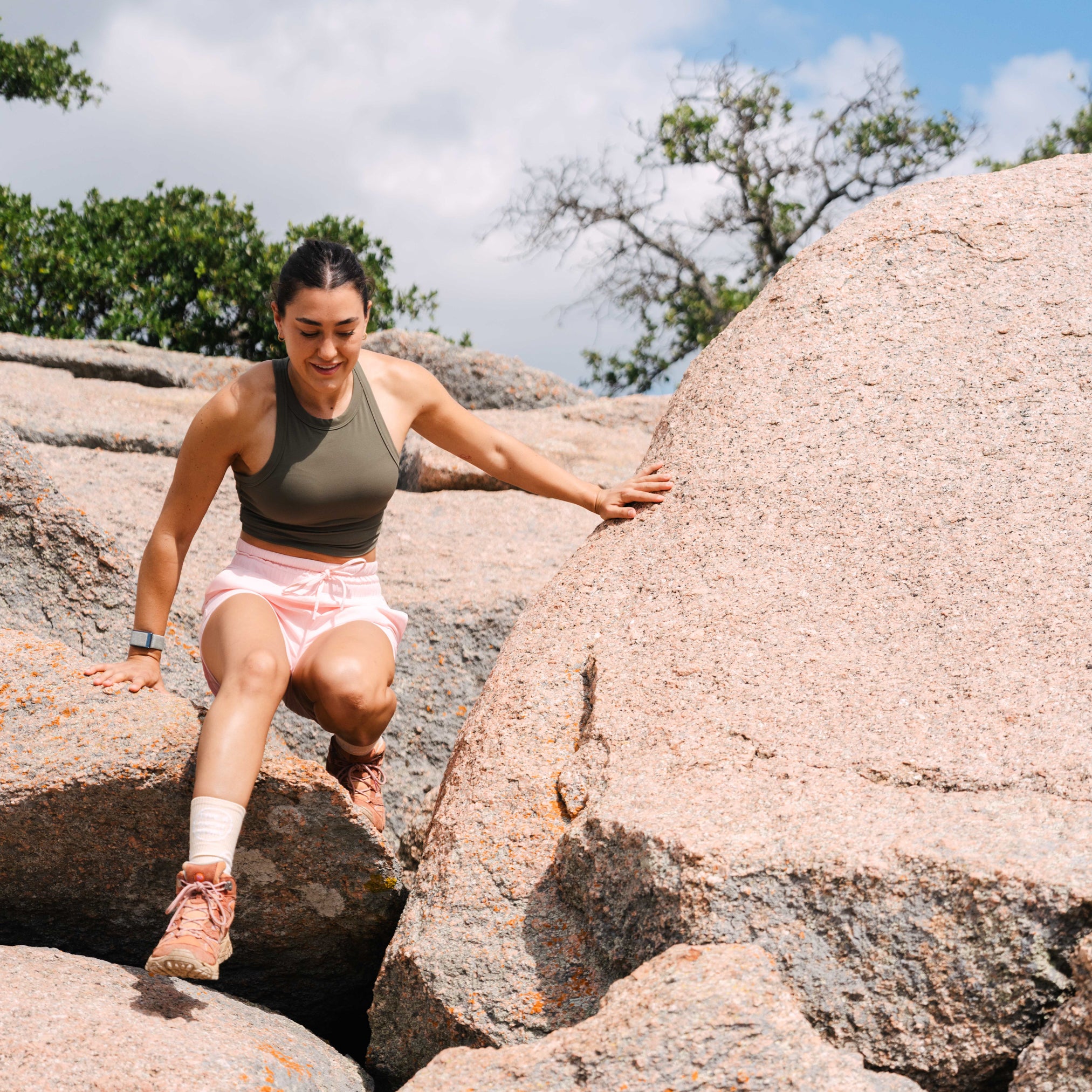 A woman wearing LIVE A GREAT STORY pink active women's shorts while climbing over a rock