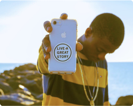 A man holding up a phone with a LIVE A GREAT STORY Inspiration Sticker on it
