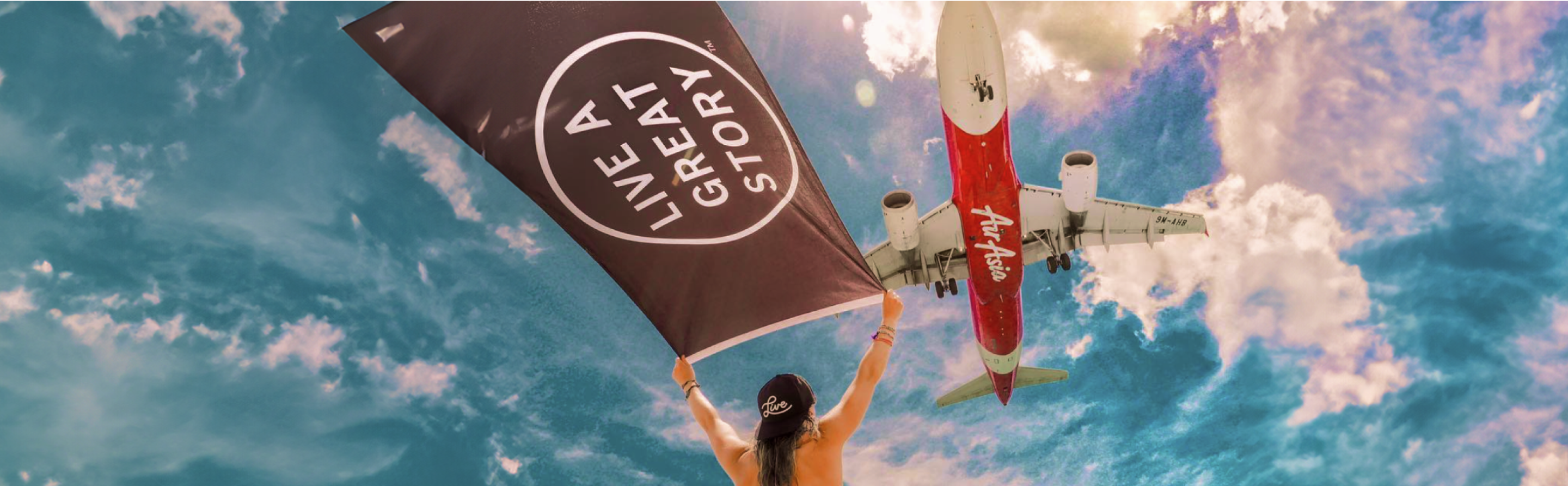 A woman holding up a LIVE A GREAT STORY Adventure Flag with an airplane flying above