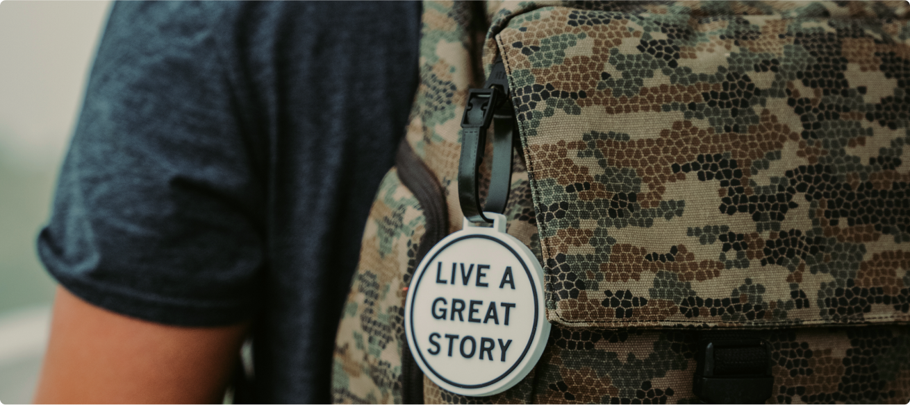 A closeup of a LIVE A GREAT STORY luggage tag on a backpack