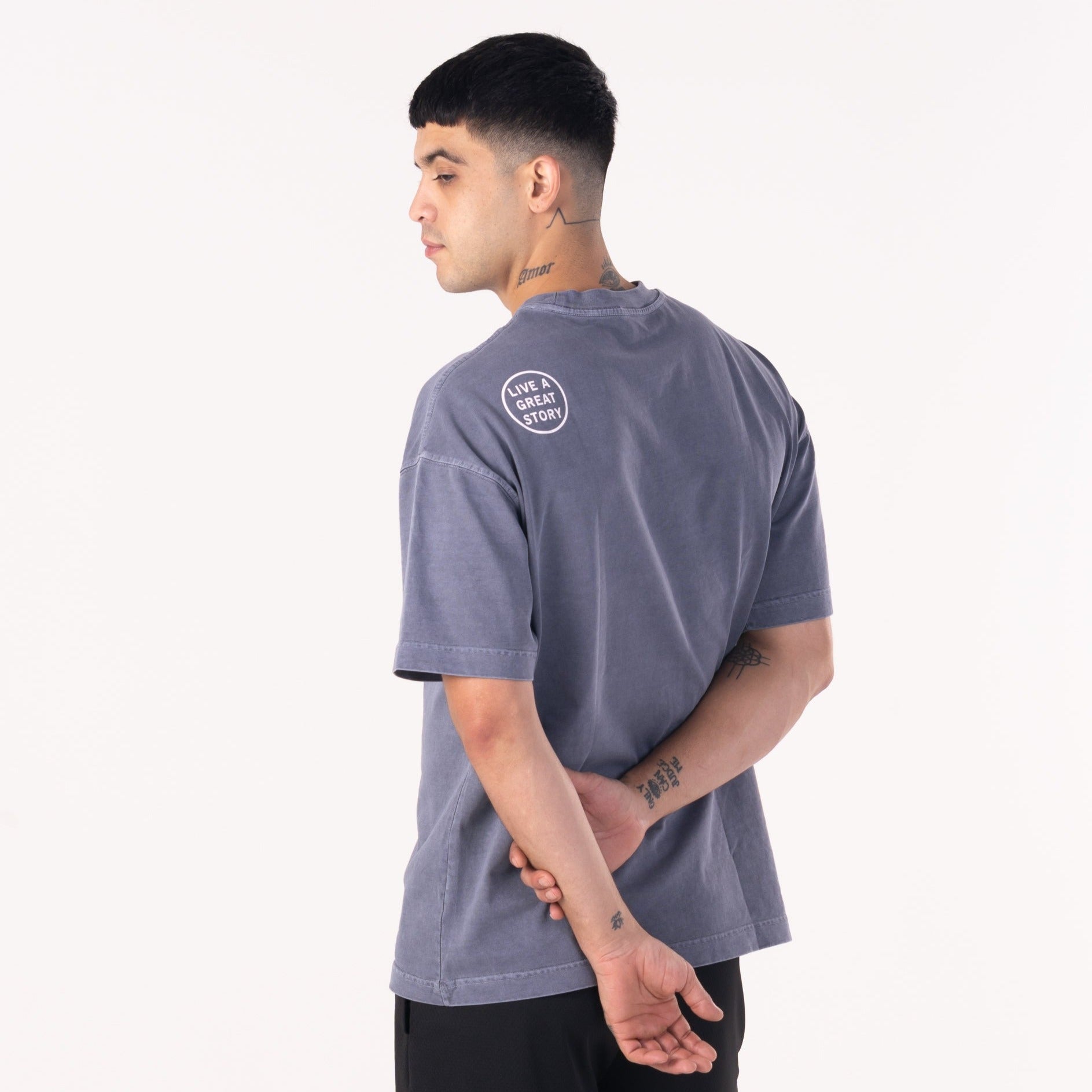 A man wearing and showing the back view of a midnight gray LIVE A GREAT STORY Shoulder Print T-shirt