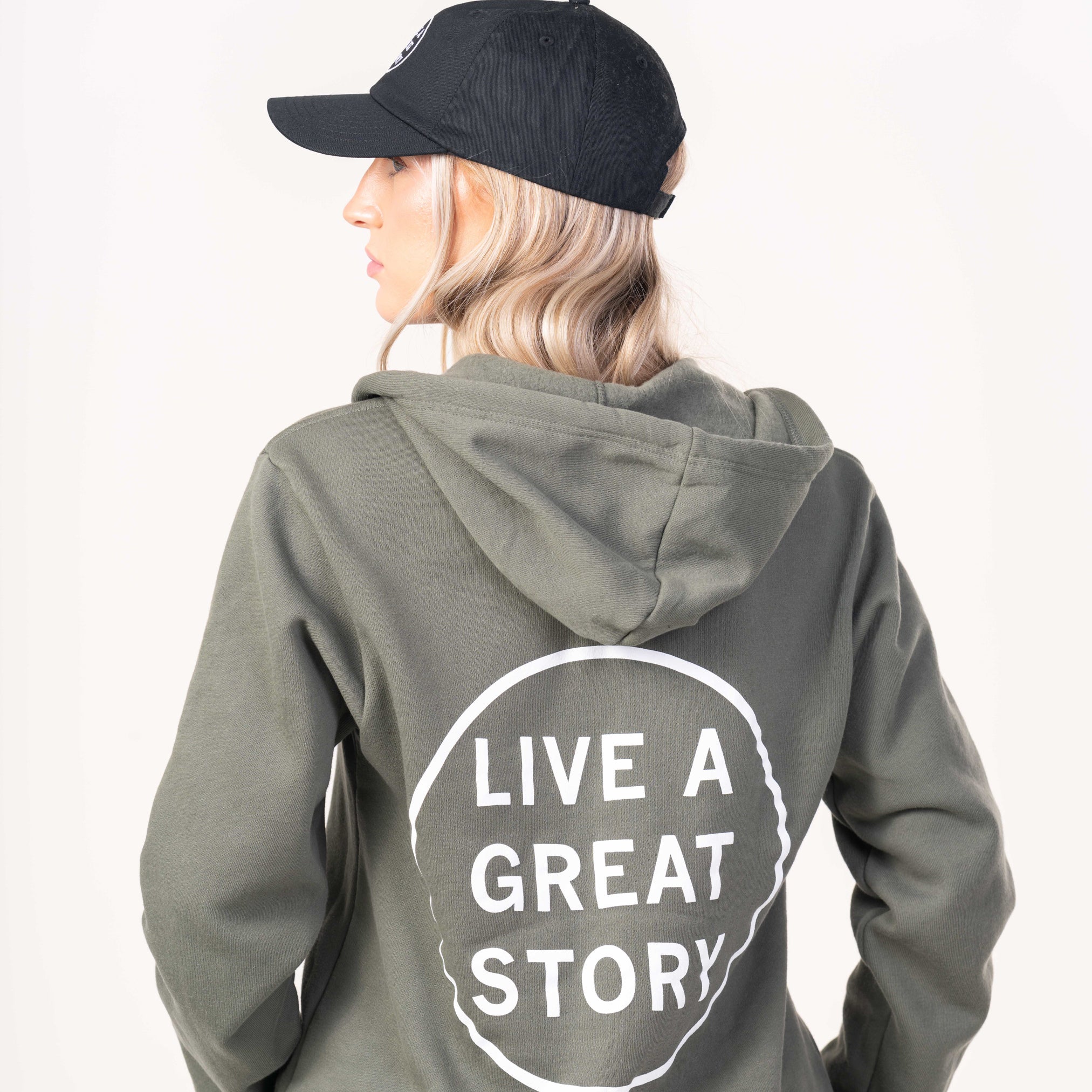 A person wearing a green LIVE A GREAT STORY zip up hoodie