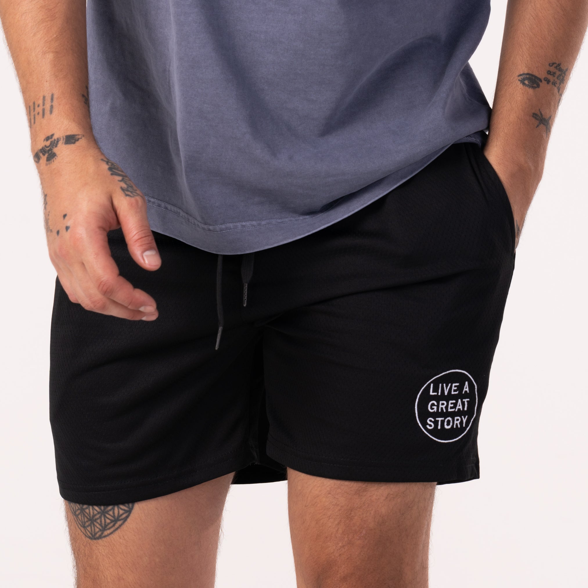 A man wearing black LIVE A GREAT STORY Men's Summer Shorts with is hand in one of the pockets