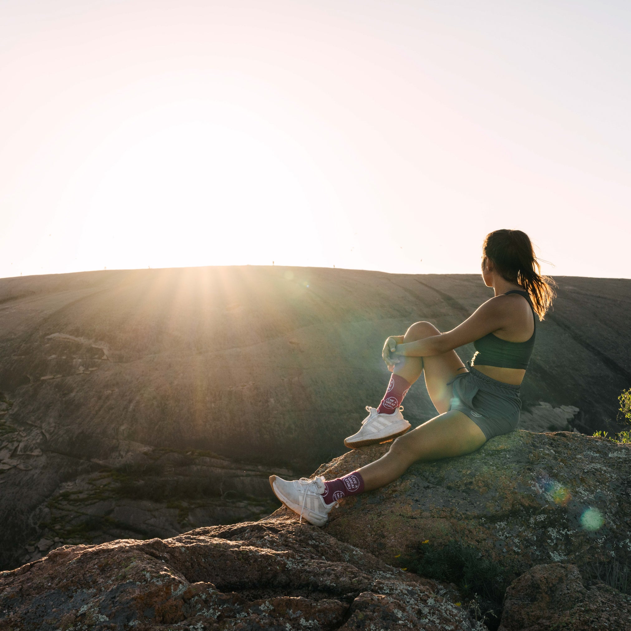 A woman wearing an olive LIVE A GREAT STORY women's tank top while outside