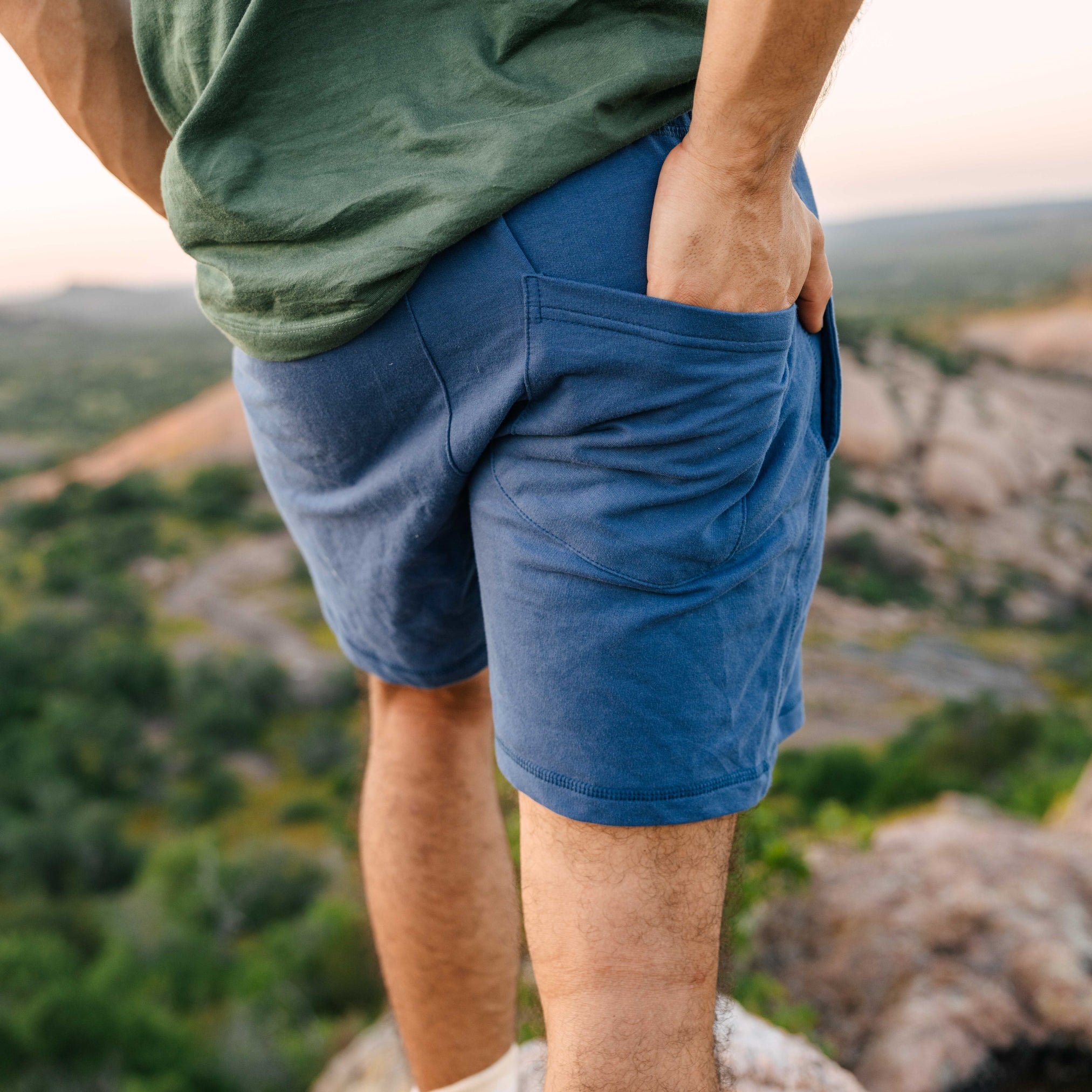 A closeup of a person wearing gray comfortable men's Camp Fire Shorts with their hand in the back pocket