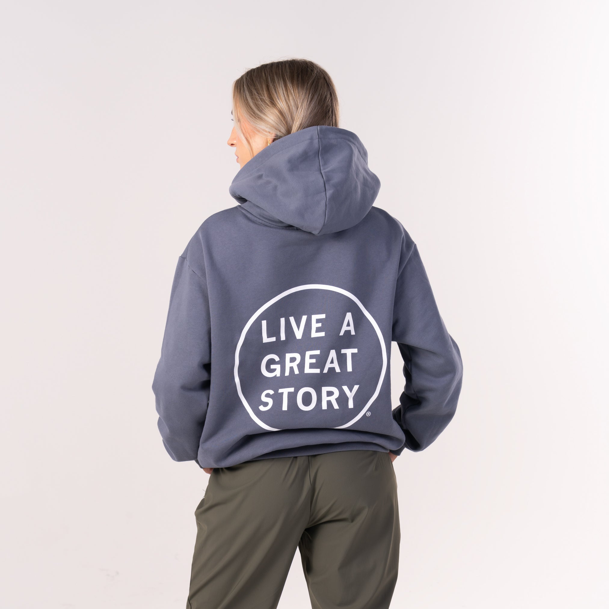 A woman wearing and showing the back of a dark gray LIVE A GREAT STORY chest and back print 100% cotton hoodie 