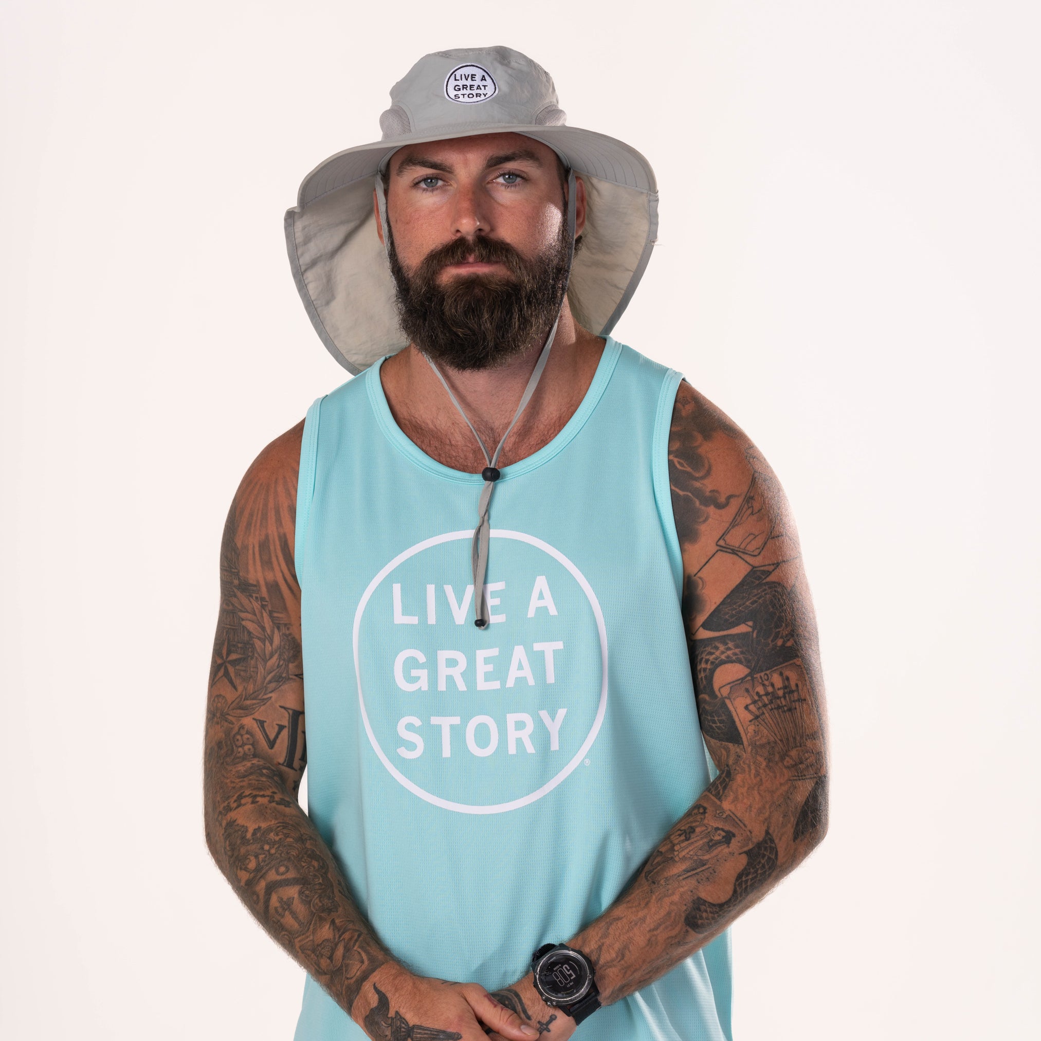 A man wearing a LIVE A GREAT STORY Adventure Hat with a LIVE A GREAT STORY men's tank top