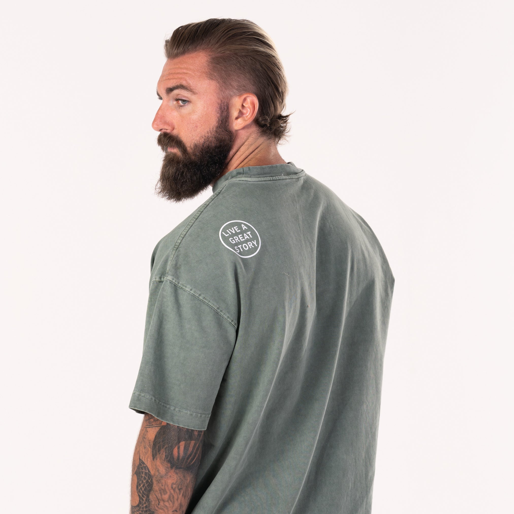 A man wearing and showing the back view of a forest green LIVE A GREAT STORY Shoulder Print T-shirt