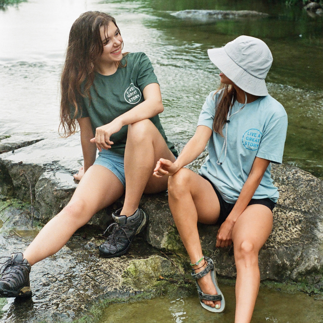 Two woman wearing a LIVE A GREAT STORY 100% cotton chest print T-shirt while outside