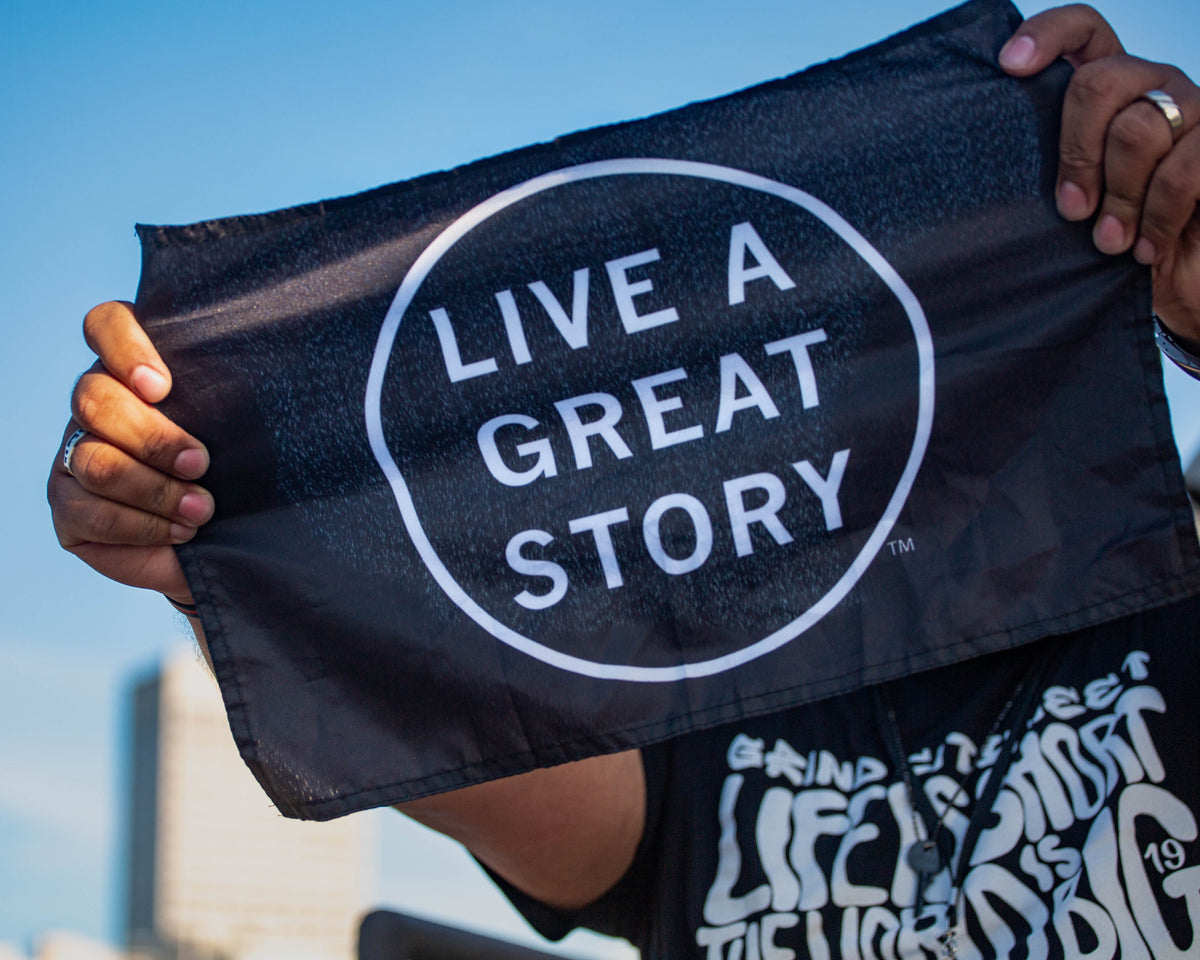 A closeup of a person holding  a black LIVE A GREAT STORY Mini Adventure Flag