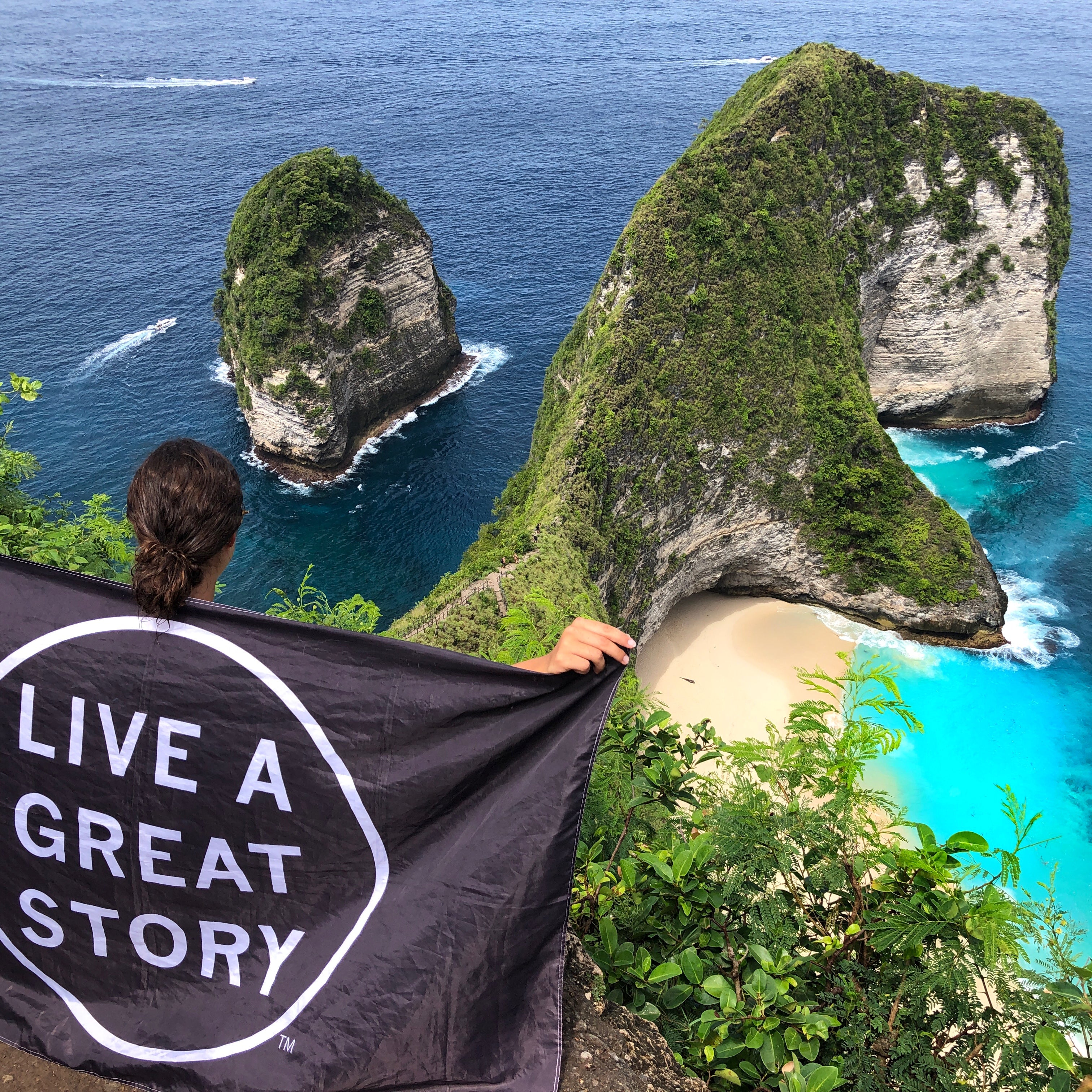 A person holding a black LIVE A GREAT STORY Adventure Flag at a scenic island