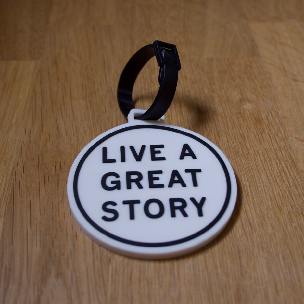 A LIVE A GREAT STORY luggage tag on a wooden surface